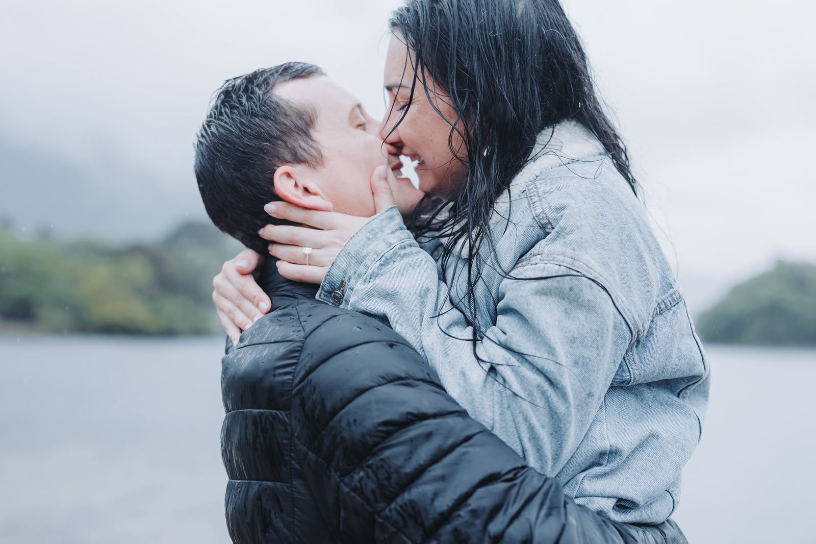 Couple sharing a passionate kiss in the rain by a misty lake