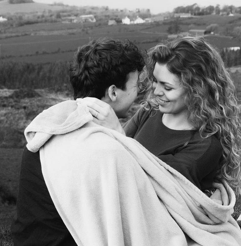 Black and white portrait of a couple smiling while wrapped in a blanket