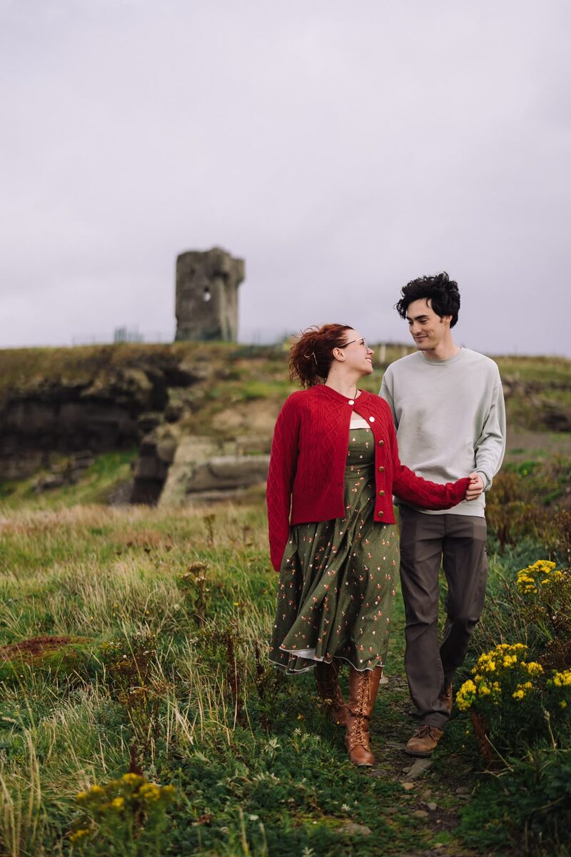 Couple walking hand in hand through a wildflower field beside an old castle ruin