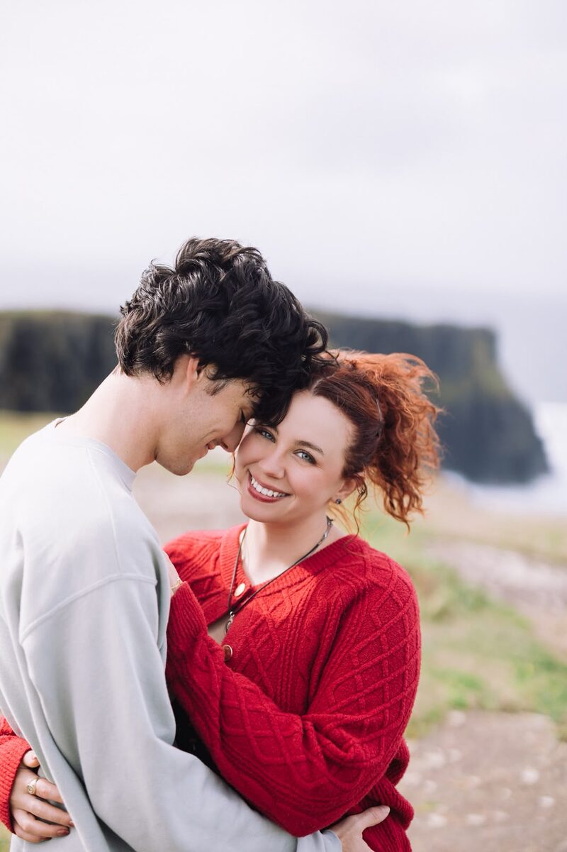 Couple standing cheek to cheek on a clifftop, smiling