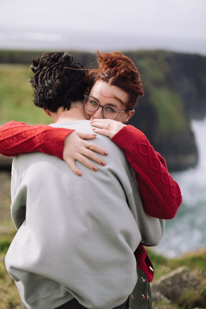 Couple holding each other close on a windy clifftop overlooking the sea