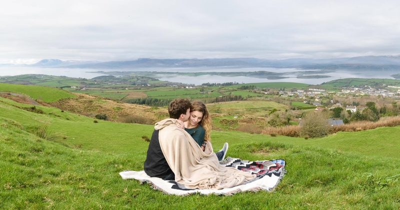 Couple wrapped in a blanket on a hilltop overlooking the coastline
