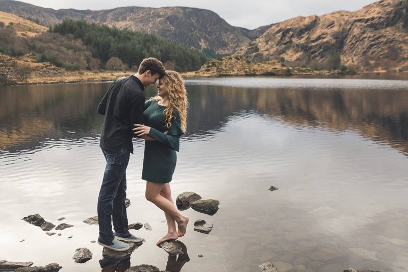 Couple embracing on the shore of a still lake surrounded by mountains