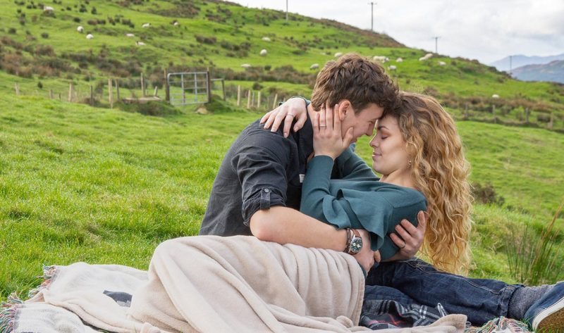Couple sitting close together on a picnic blanket in a hillside field