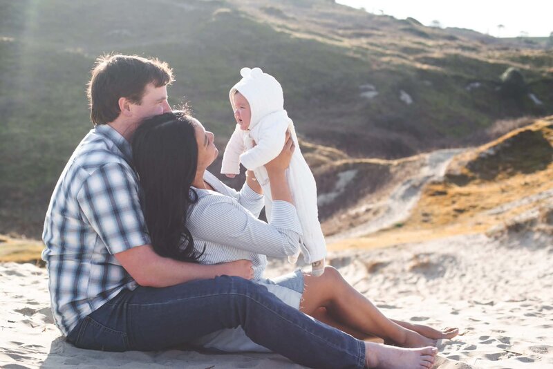 Parents holding their baby up together on a sunlit beach