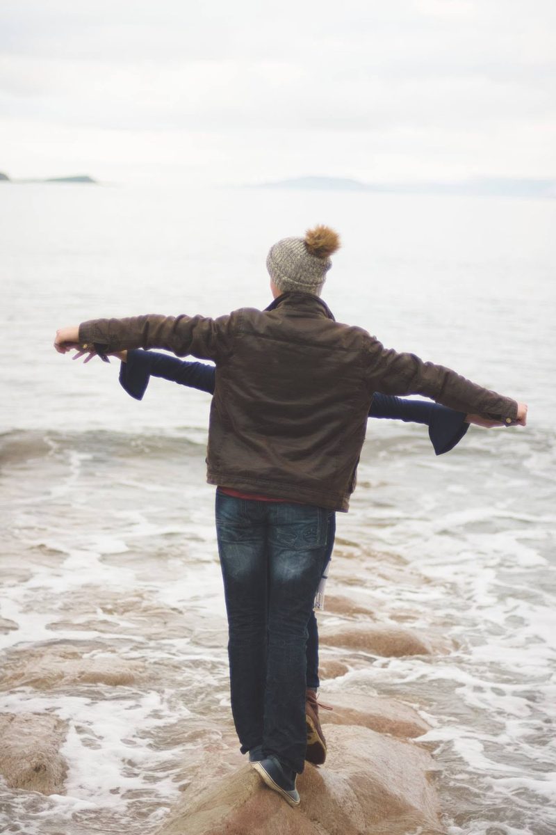 Woman standing on a coastal rock with arms outstretched toward the sea
