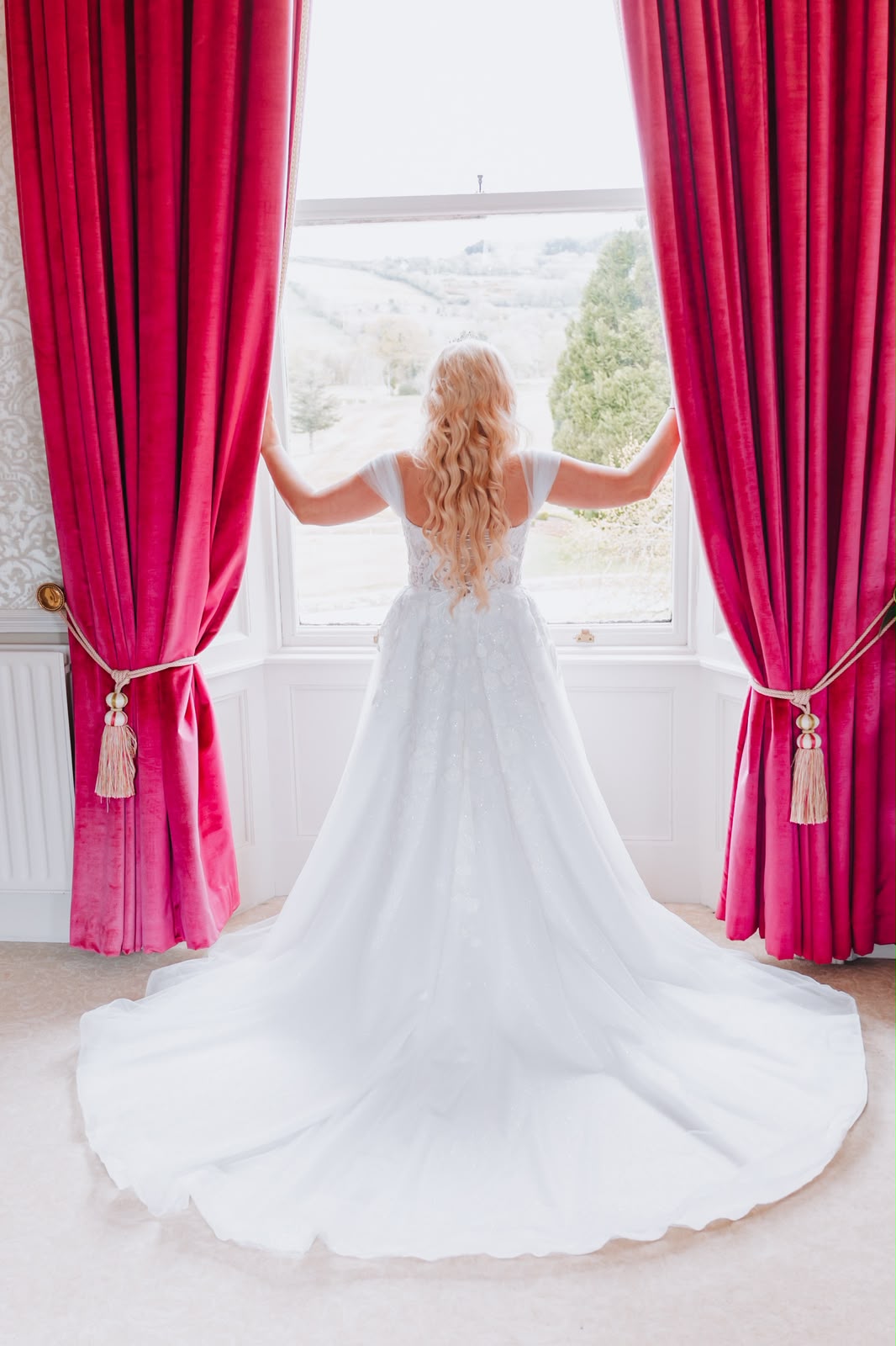 Bride in wedding dress at a window with red curtains