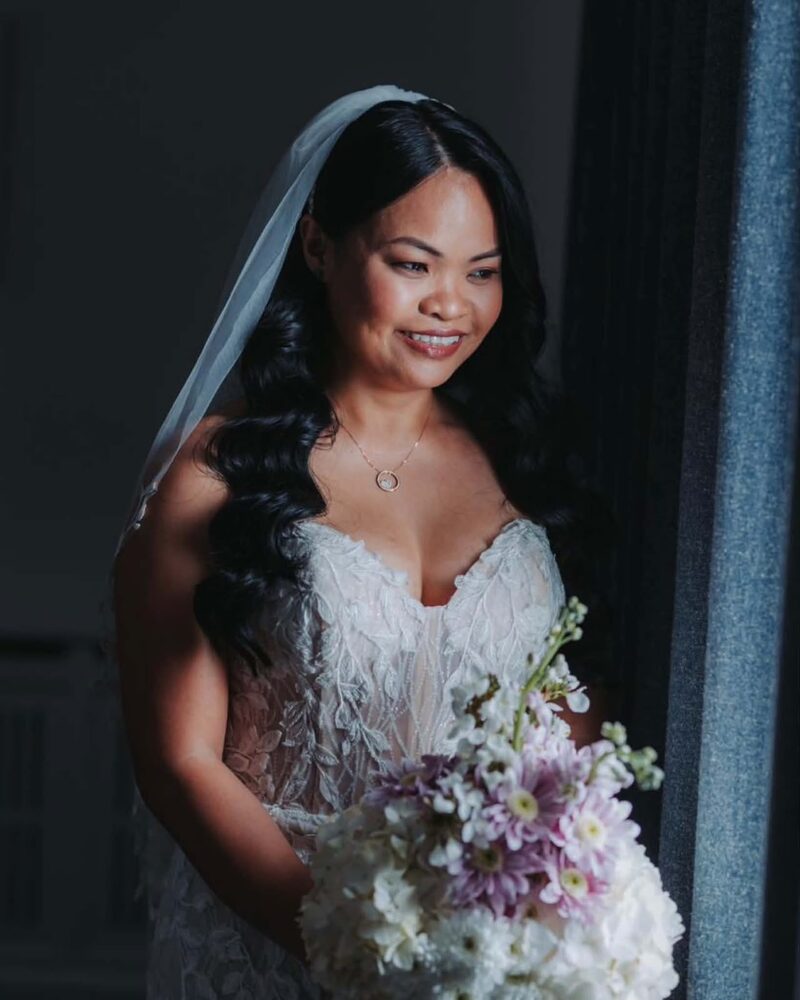 Bride smiling in soft window light, holding a pastel bouquet