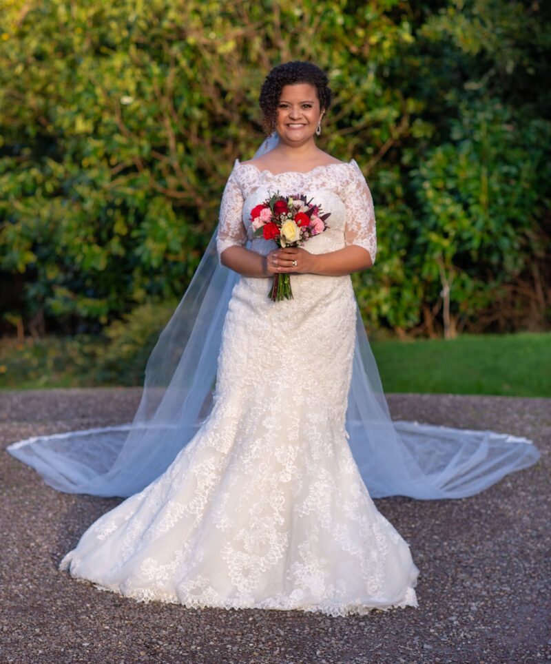 Bride standing in a garden holding her bouquet, full-length portrait with a soft blue veil